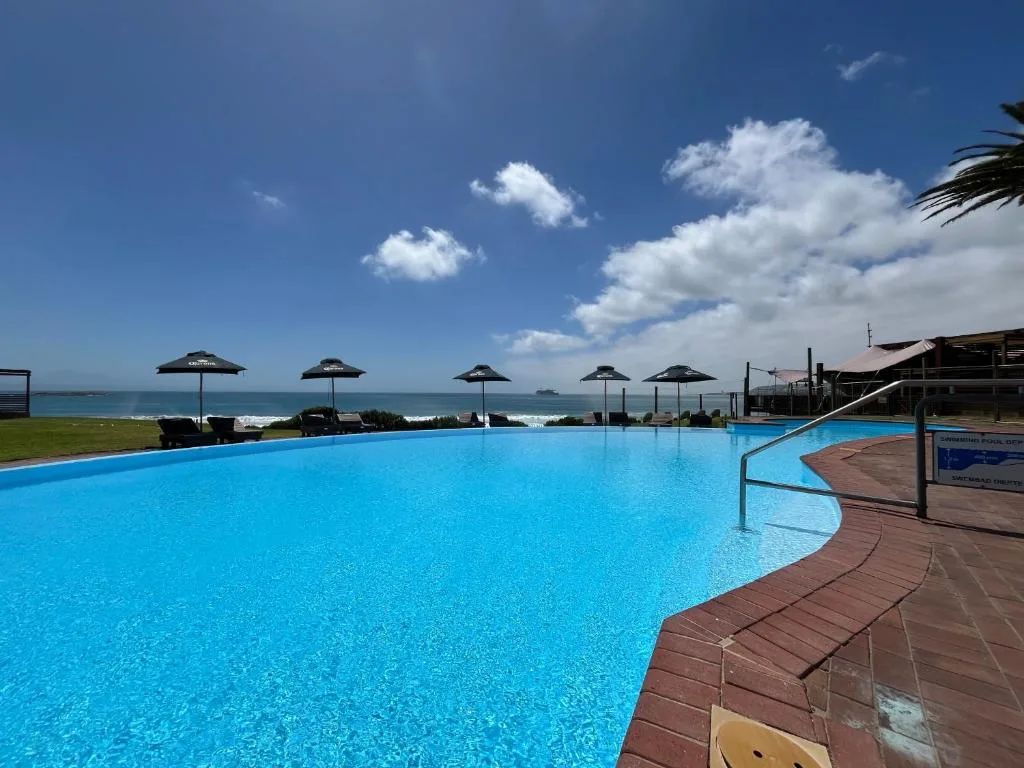 Large curved swimming pool overlooking the ocean with black umbrellas and loungers