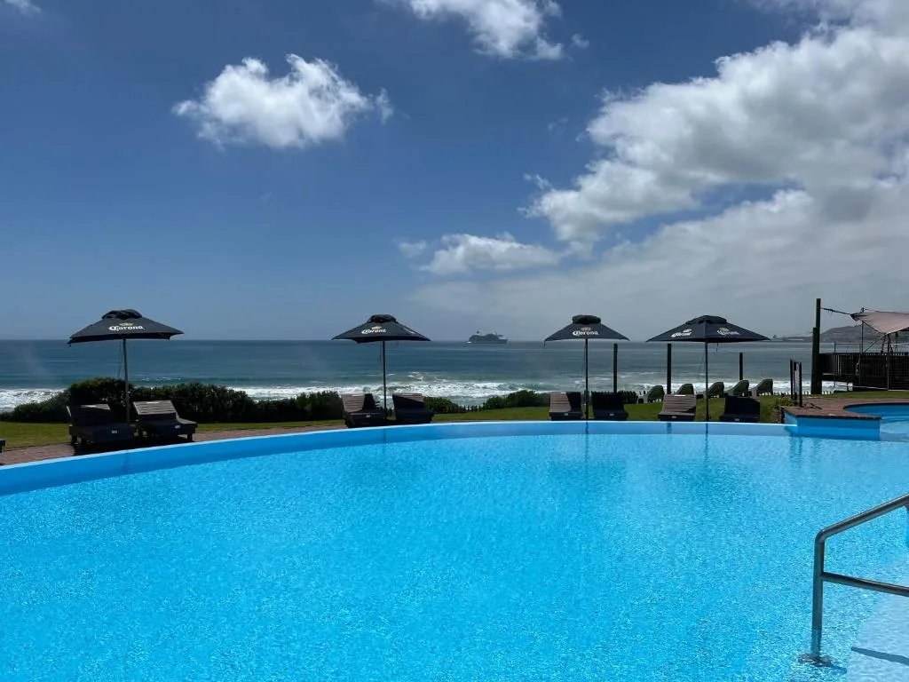 Large swimming pool with ocean view, umbrellas, and beachfront beyond