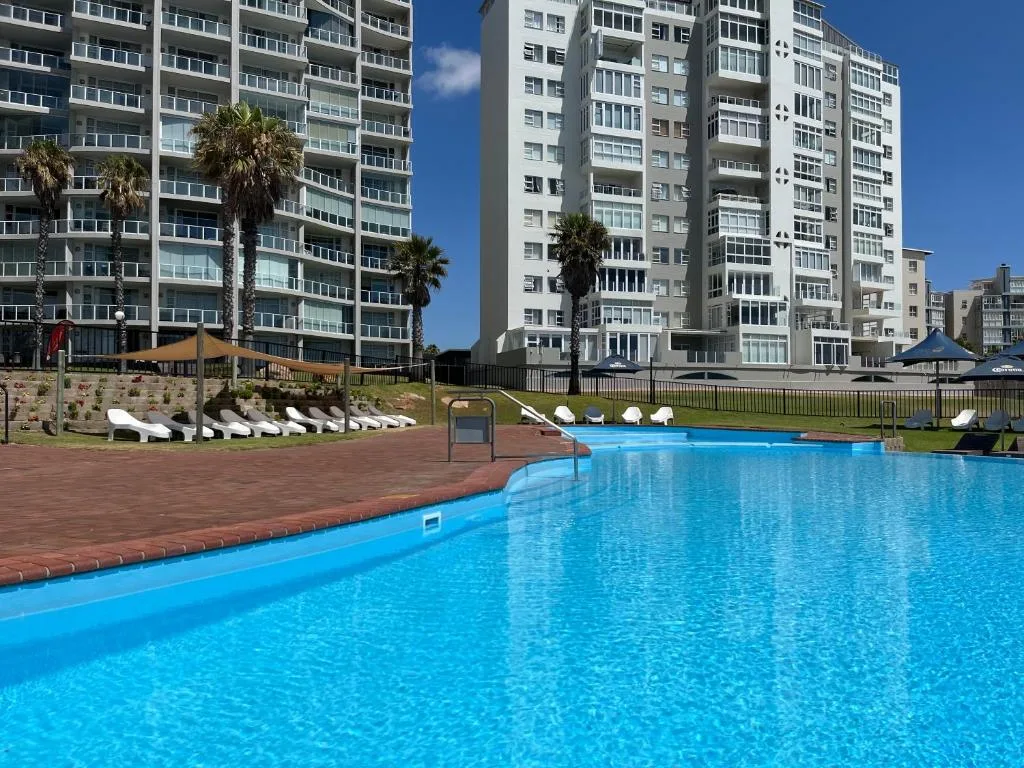 Bright blue swimming pool with white loungers and coastal apartment buildings