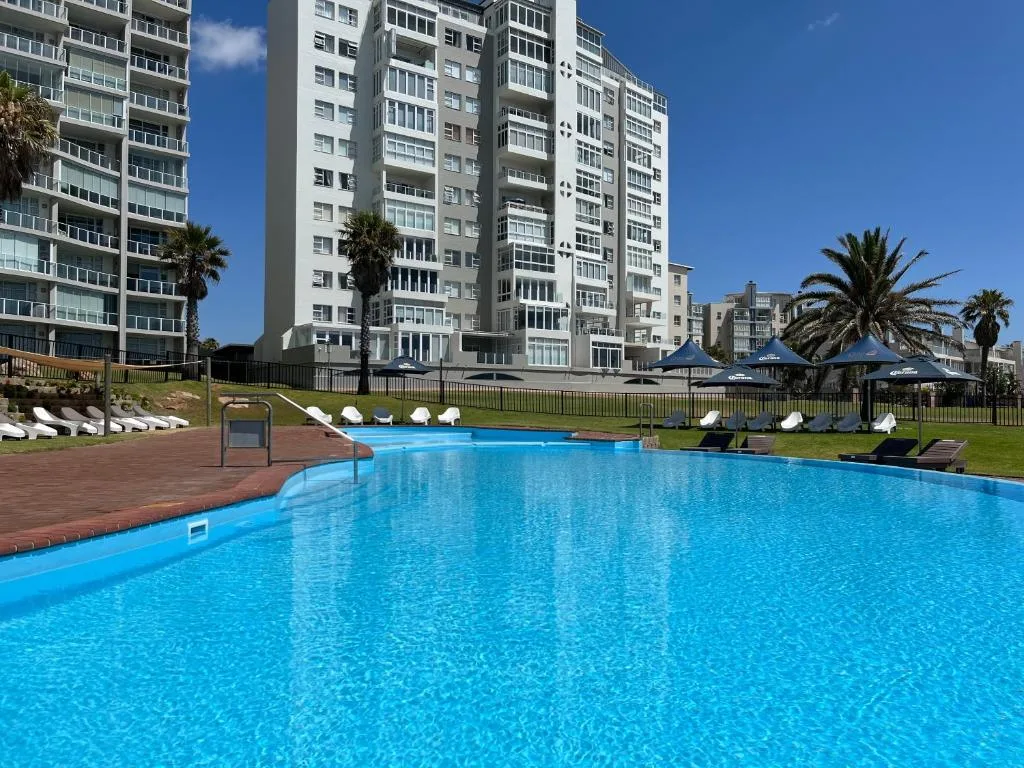 Sparkling blue swimming pool with loungers and palm trees, apartment building backdrop
