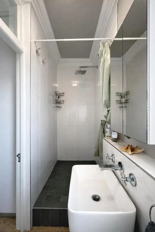 Modern bathroom with white tiles, vanity sink, and walk-in shower enclosure