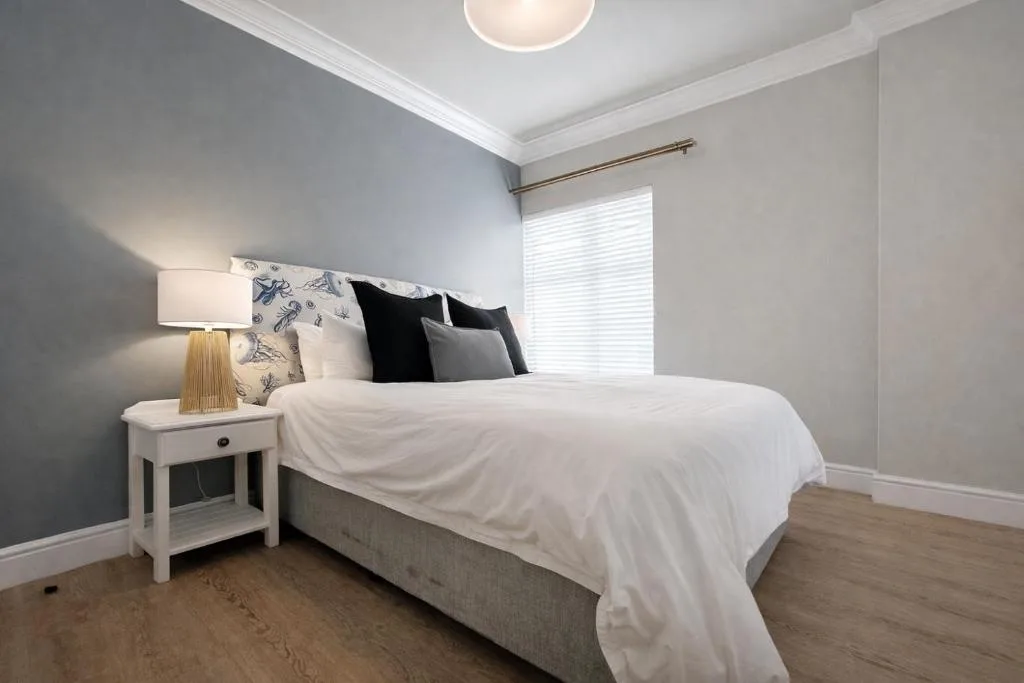Bright bedroom with queen bed, white nightstand, and soft blue accent wall