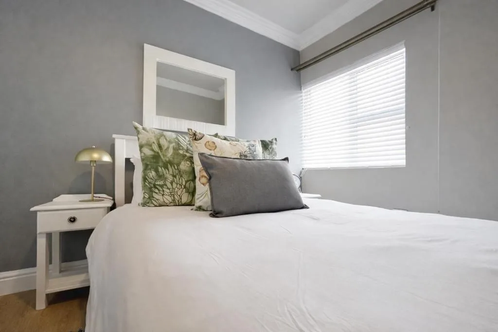 Modern bedroom with white bedding, decorative pillows, and contemporary nightstand lamp