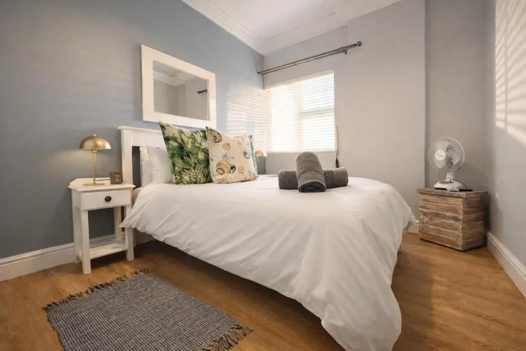 Bright bedroom with white bed, nightstands, and large windows with natural light