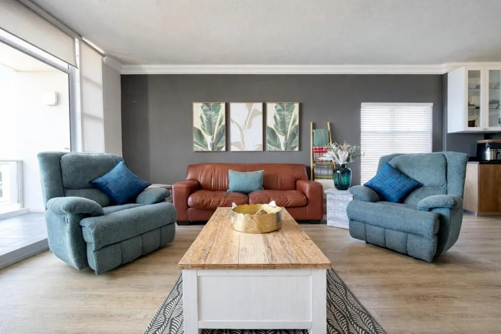 Modern lounge with blue recliners, rust sofa, wooden coffee table, and botanical wall art