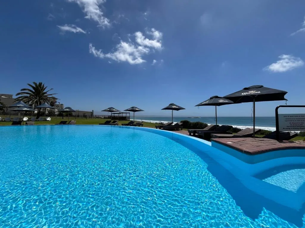 Large sparkling blue swimming pool overlooking the ocean and beach on a clear day