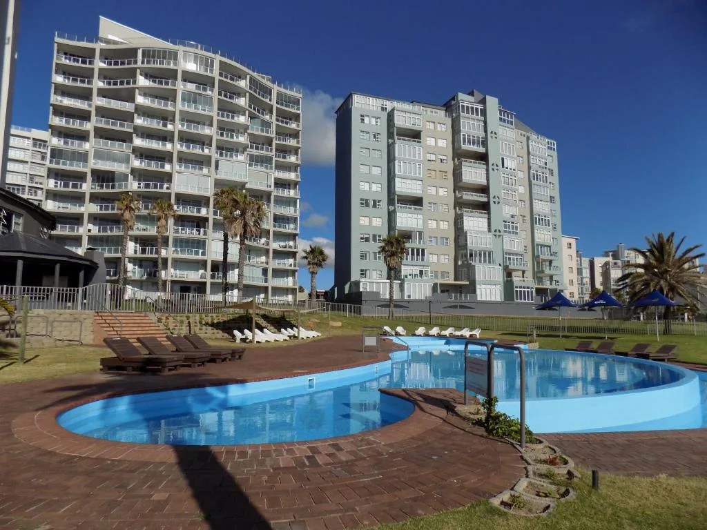 Curved swimming pool with loungers overlooking beachfront apartment buildings