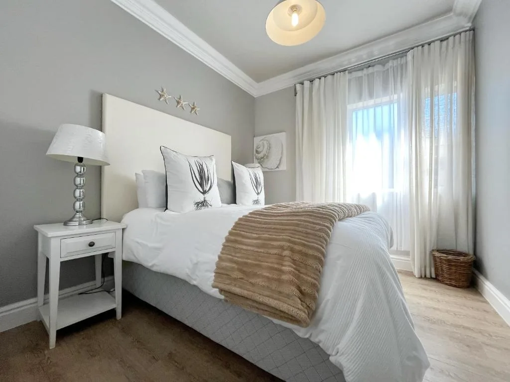 Bright bedroom with queen bed, white headboard, and cream bedding with throw