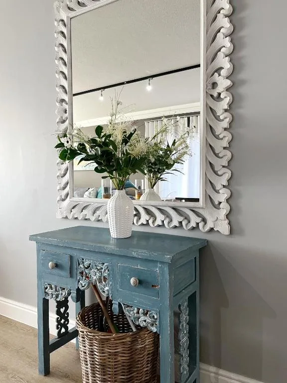 Ornate white-framed mirror above blue vintage console table with fresh flowers