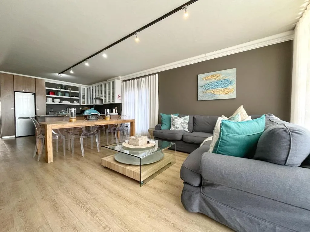 Modern open-plan lounge with gray sofas and teal cushions overlooking kitchen