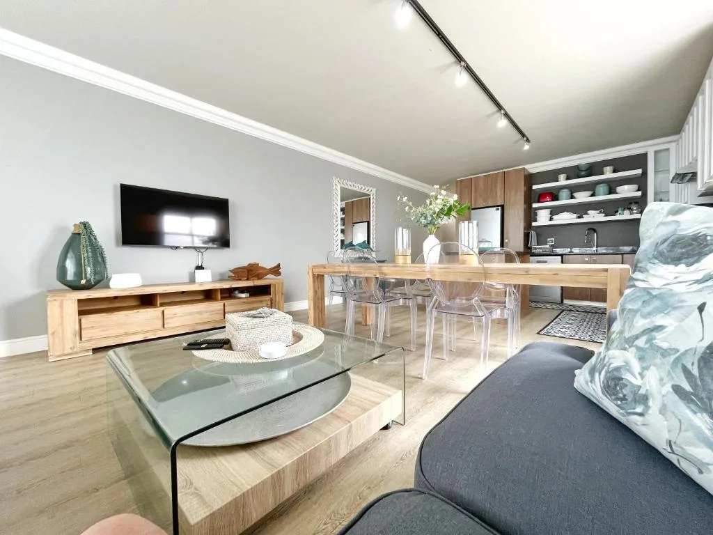 Modern open-plan lounge with TV, wooden furniture, and dining area beyond