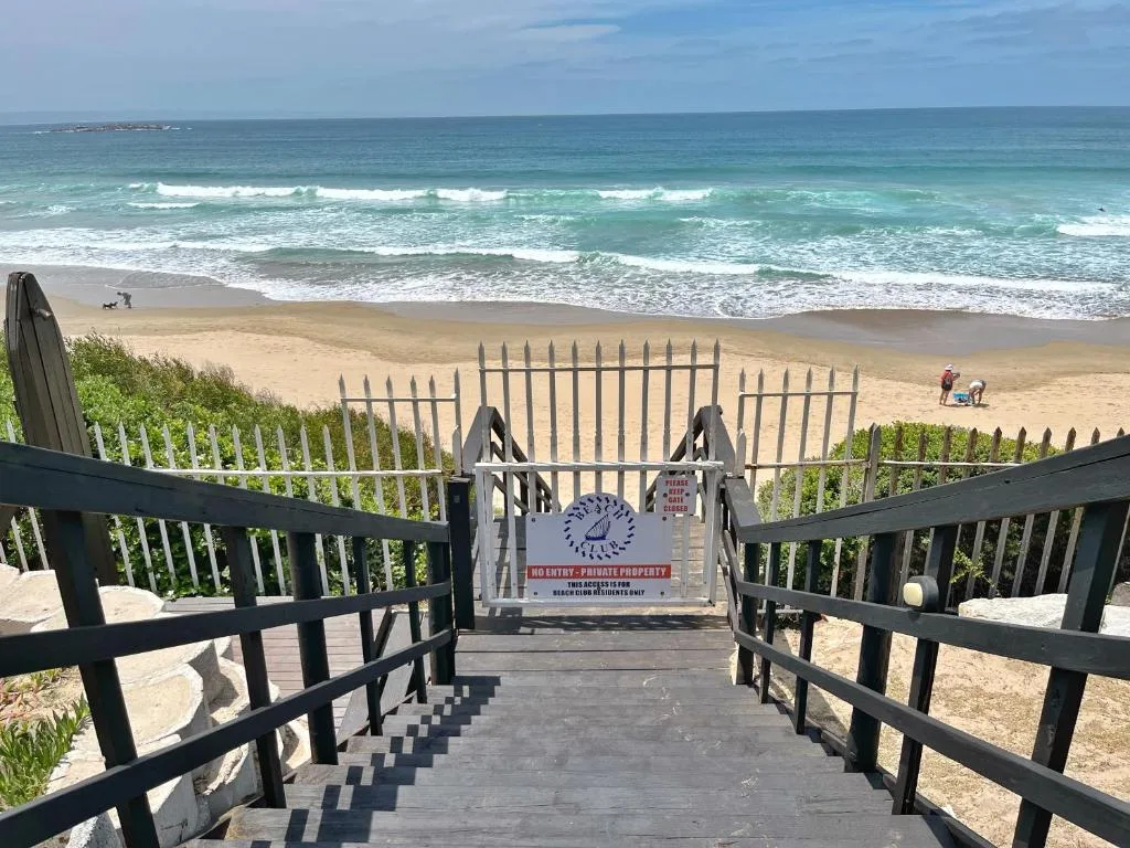 Ocean beach view with waves and sand accessed via wooden boardwalk stairs