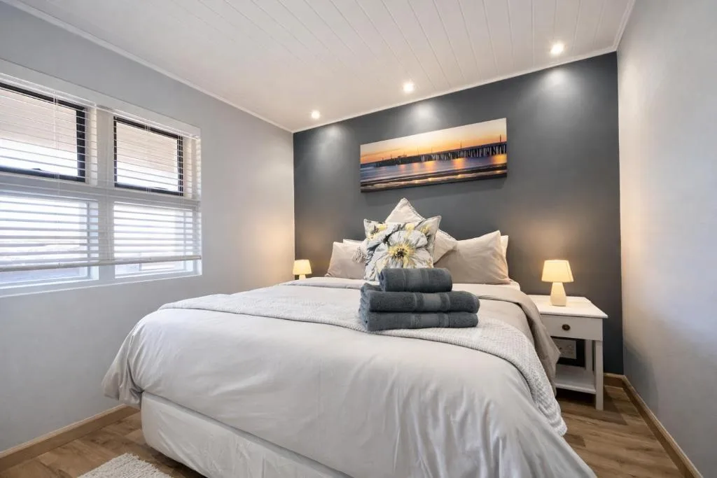 Modern bedroom with queen bed, dark accent wall, and coastal artwork