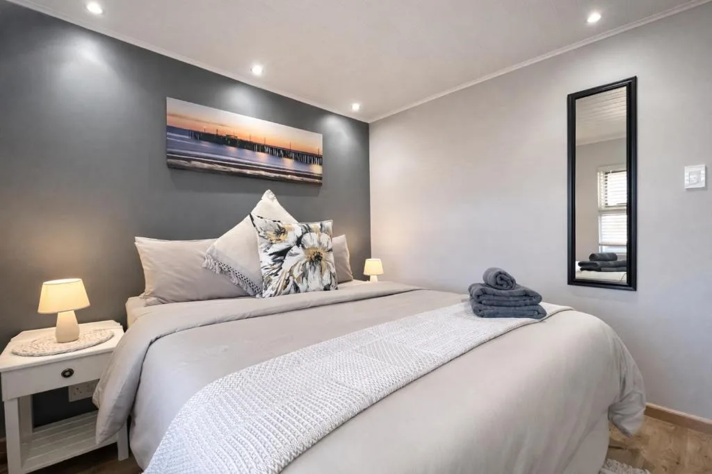 Modern bedroom with queen bed, grey accent wall, coastal artwork, and folded towels