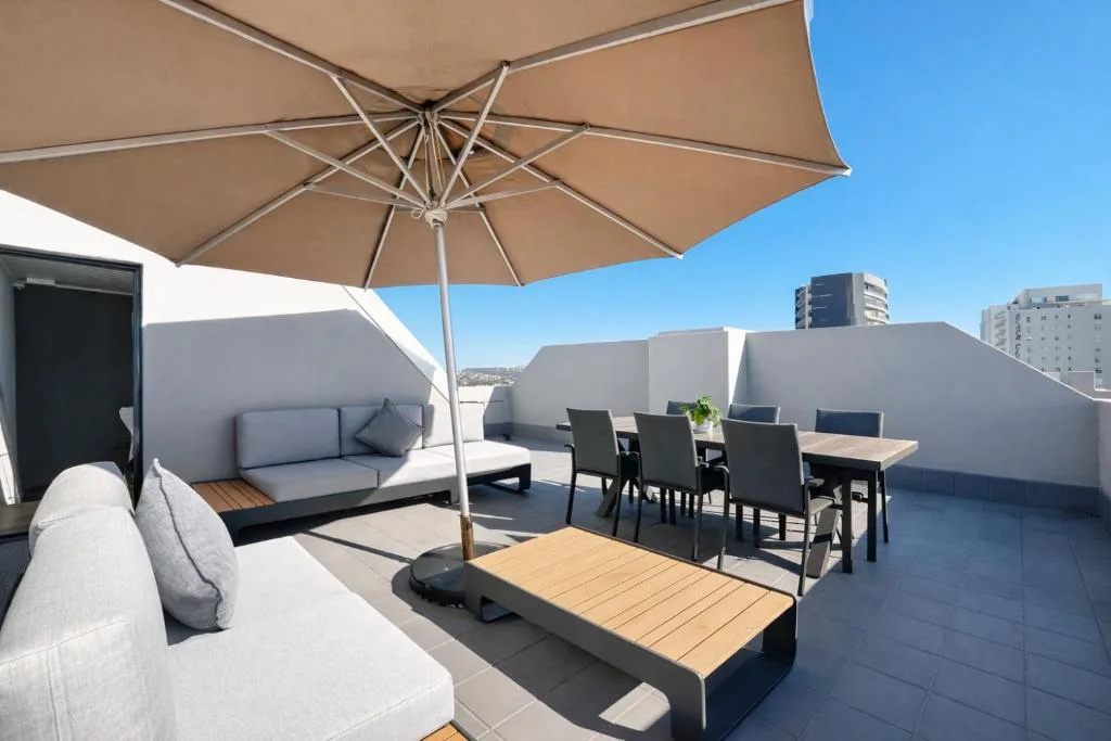 Spacious rooftop deck with lounge seating, dining table, and large umbrella