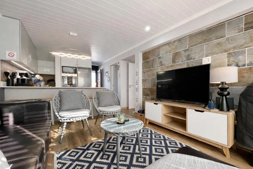 Modern lounge with TV, comfortable seating, kitchen area visible