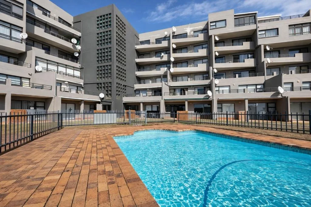 Crystal clear swimming pool with wooden deck and modern apartment complex