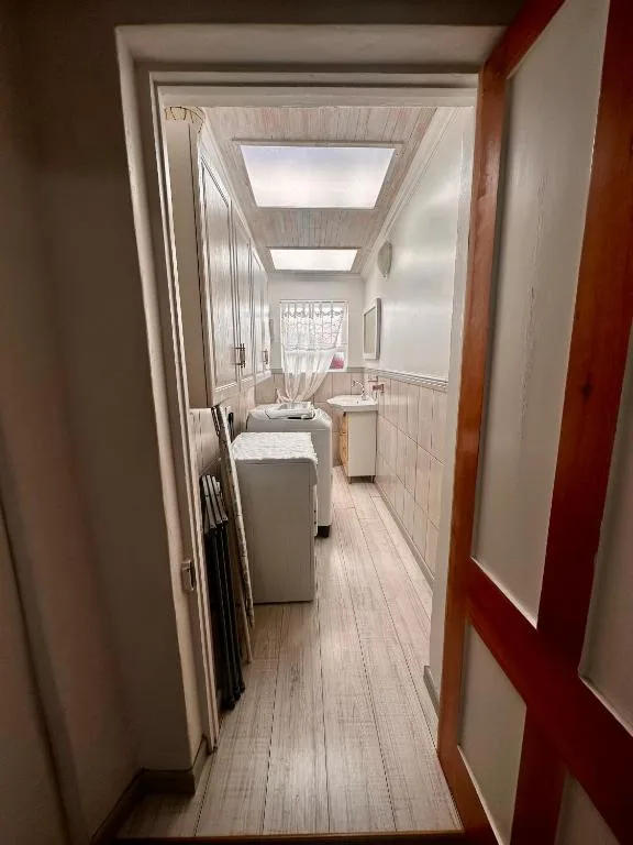 Narrow bathroom with skylight, washing machine, and white tile walls