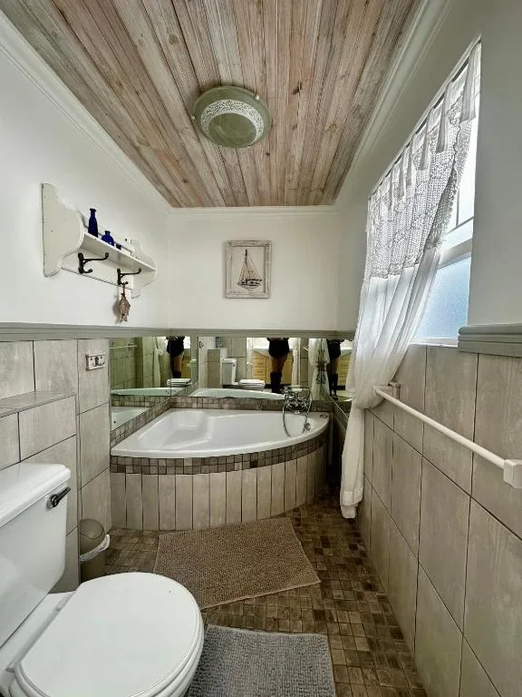 Spacious bathroom with corner bathtub, toilet, vanity and wooden ceiling