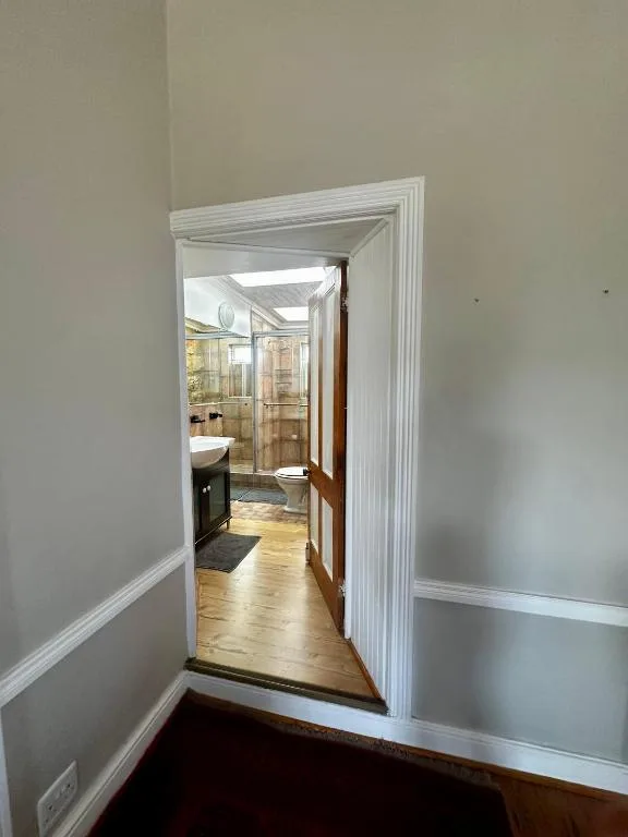 Modern bathroom with glass shower enclosure and wooden flooring visible through doorway