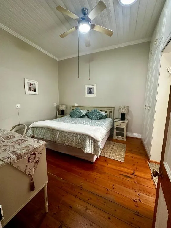 Spacious bedroom with queen bed, ceiling fan, wooden floors, and natural light