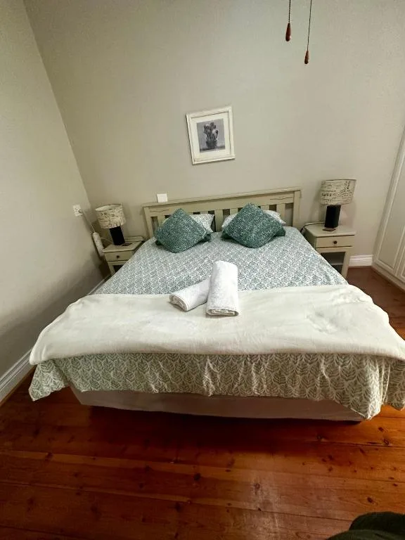 Bright bedroom with neatly made bed, green cushions, and wooden bedside tables
