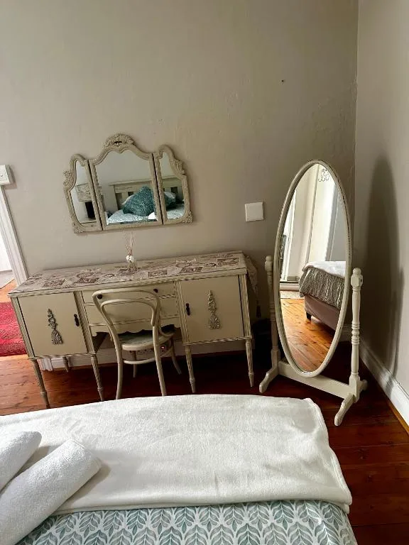 Bedroom with vintage vanity, ornate mirrors, and wooden floorboards