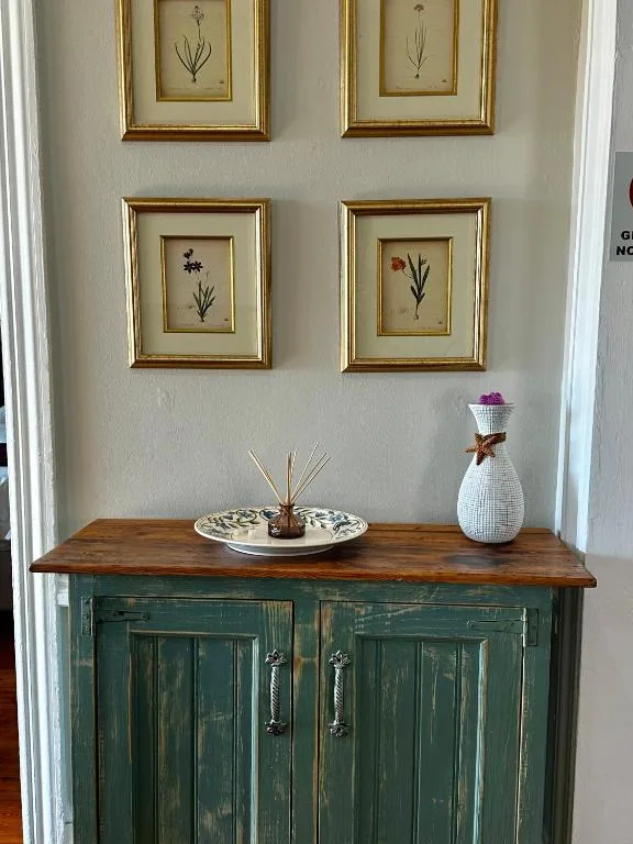 Vintage green cabinet with framed botanical prints and decorative vase