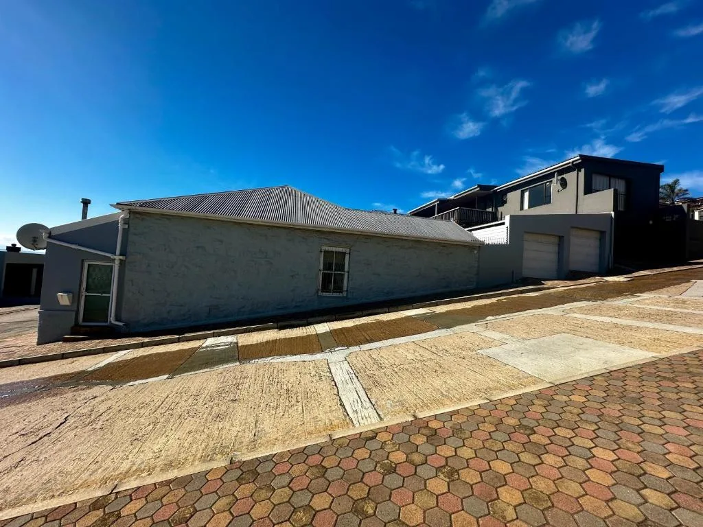 White cottage with corrugated roof and paved driveway under blue sky