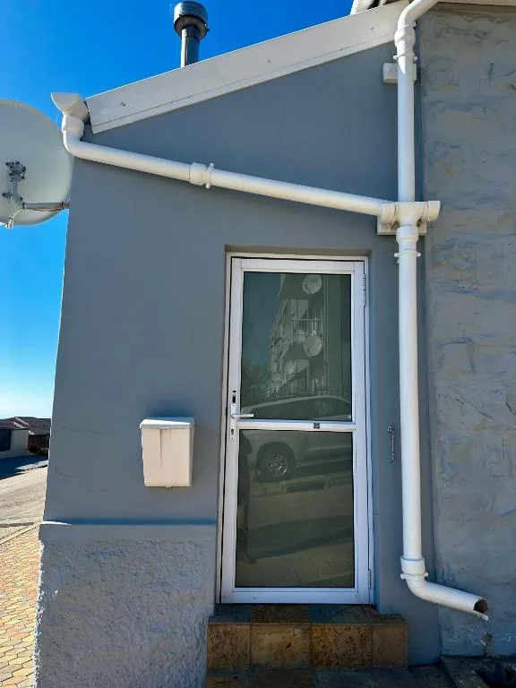 Modern cottage entrance with blue-grey walls and white door under clear sky