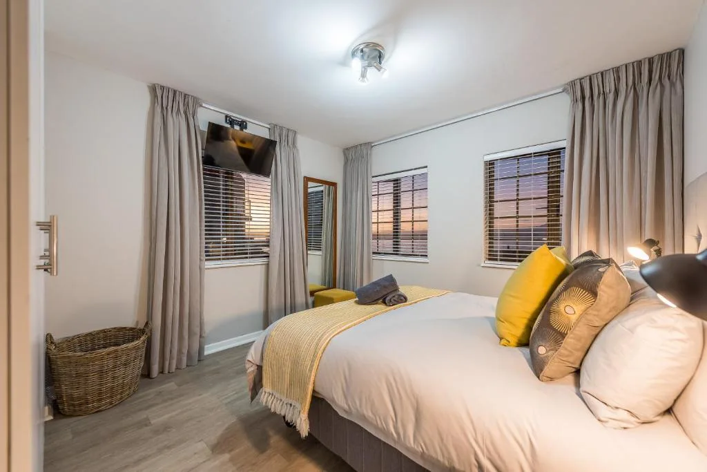 Bright bedroom with queen bed, yellow accents, TV, and sunset views through windows