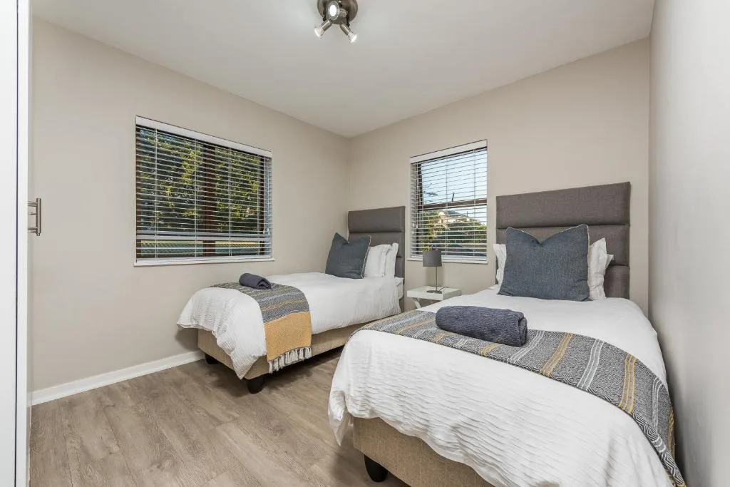 Twin bedroom with two single beds, grey headboards, white linens, natural light