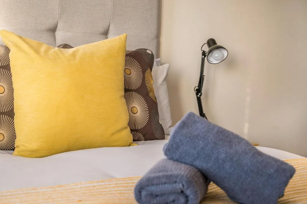 Bedroom with yellow pillow, patterned cushions, and bedside lamp