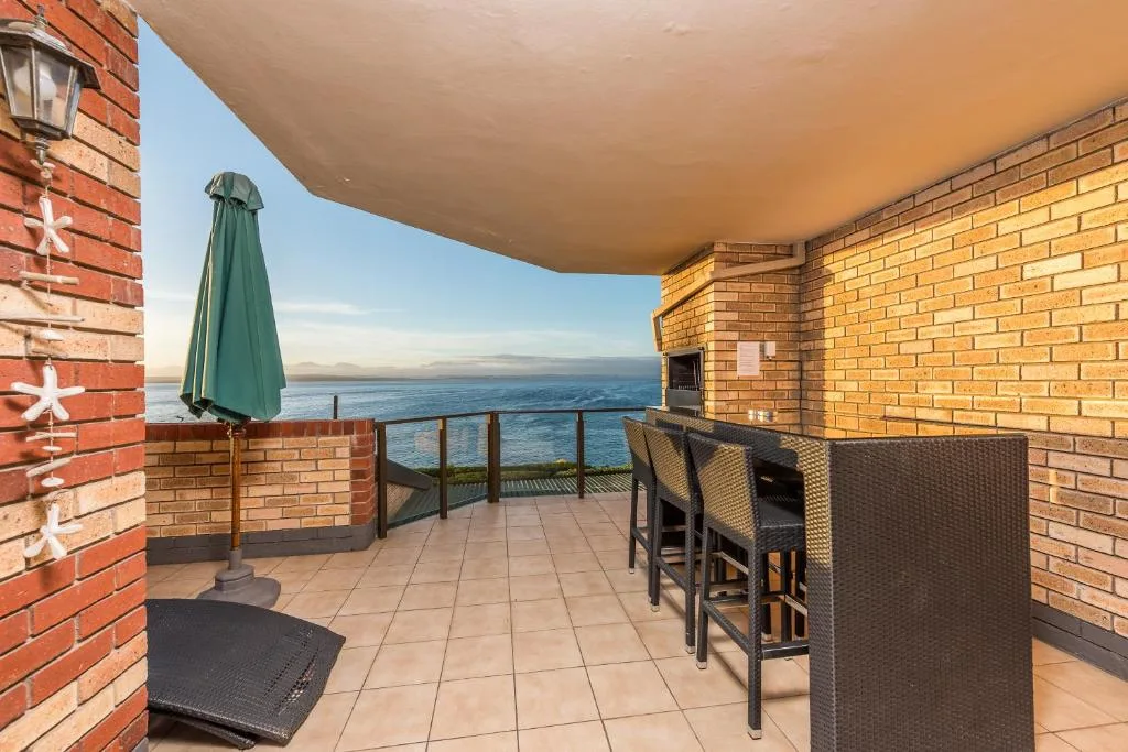 Covered oceanfront deck with bar seating and green umbrella overlooking sea