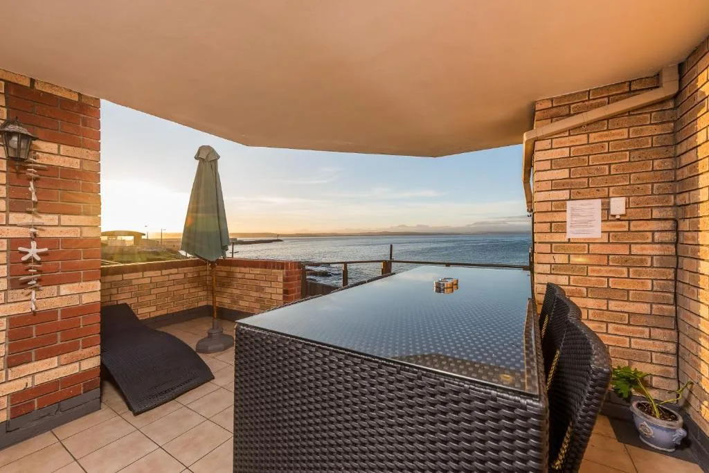 Waterfront deck with table, umbrella, and ocean views at sunset