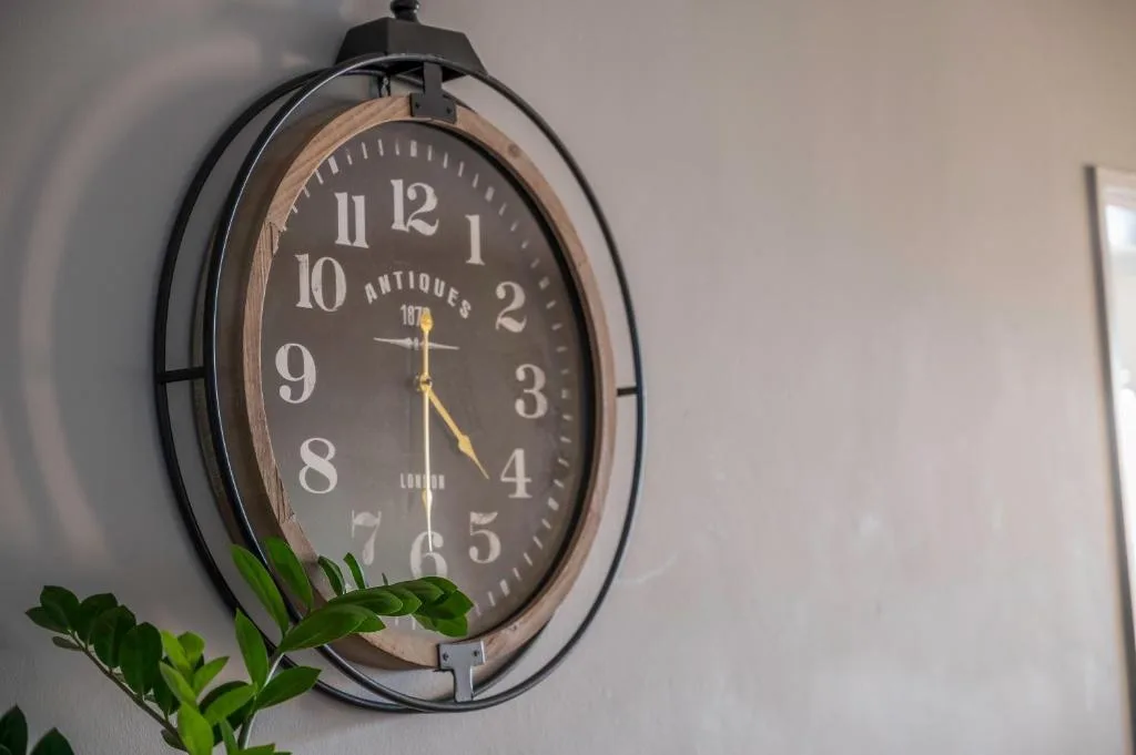 Vintage-style antiques wall clock with brass hands and green foliage