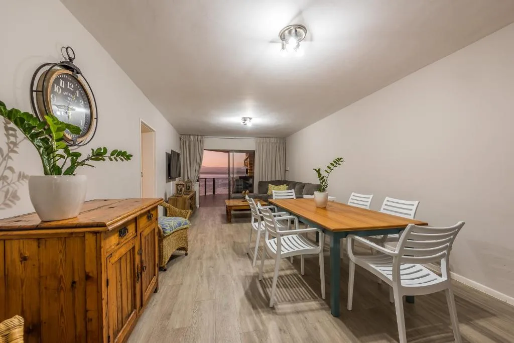 Spacious dining area with wooden table and white chairs overlooking sunset