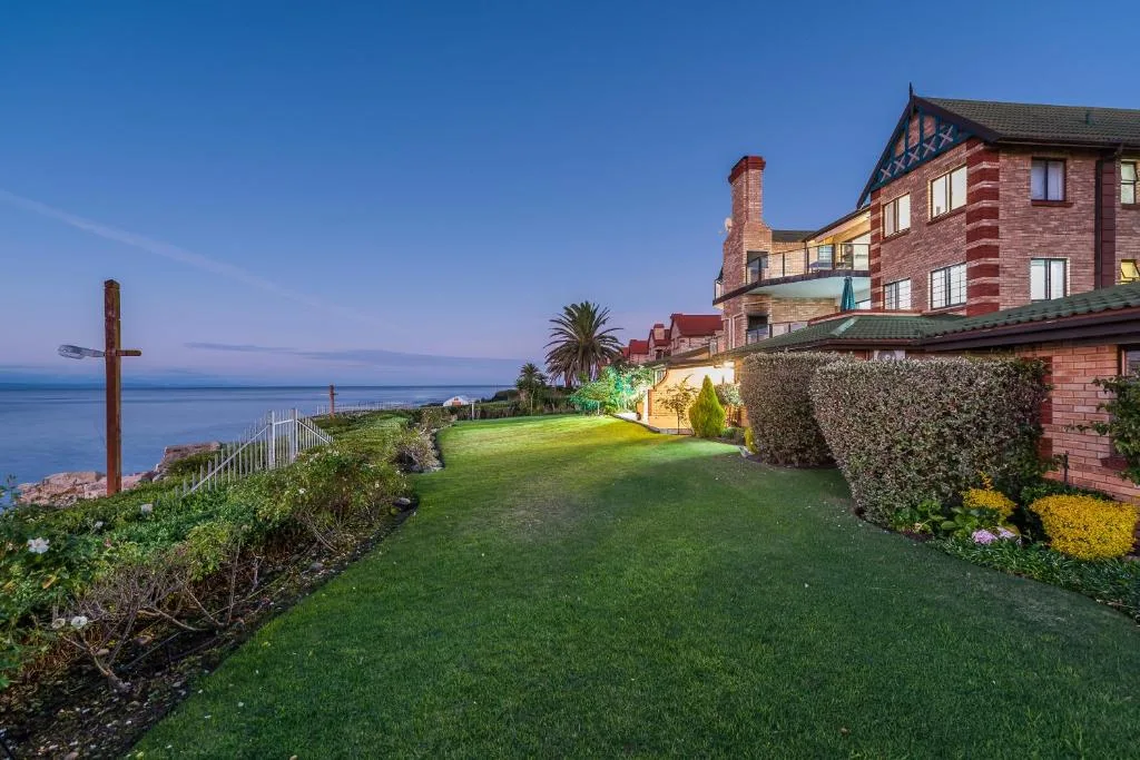 Grand brick Victorian building with manicured lawn overlooking ocean at dusk