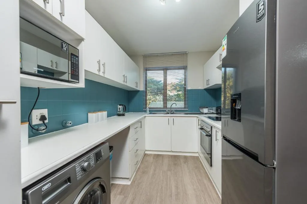 Modern kitchen with white cabinetry, teal backsplash, stainless steel appliances