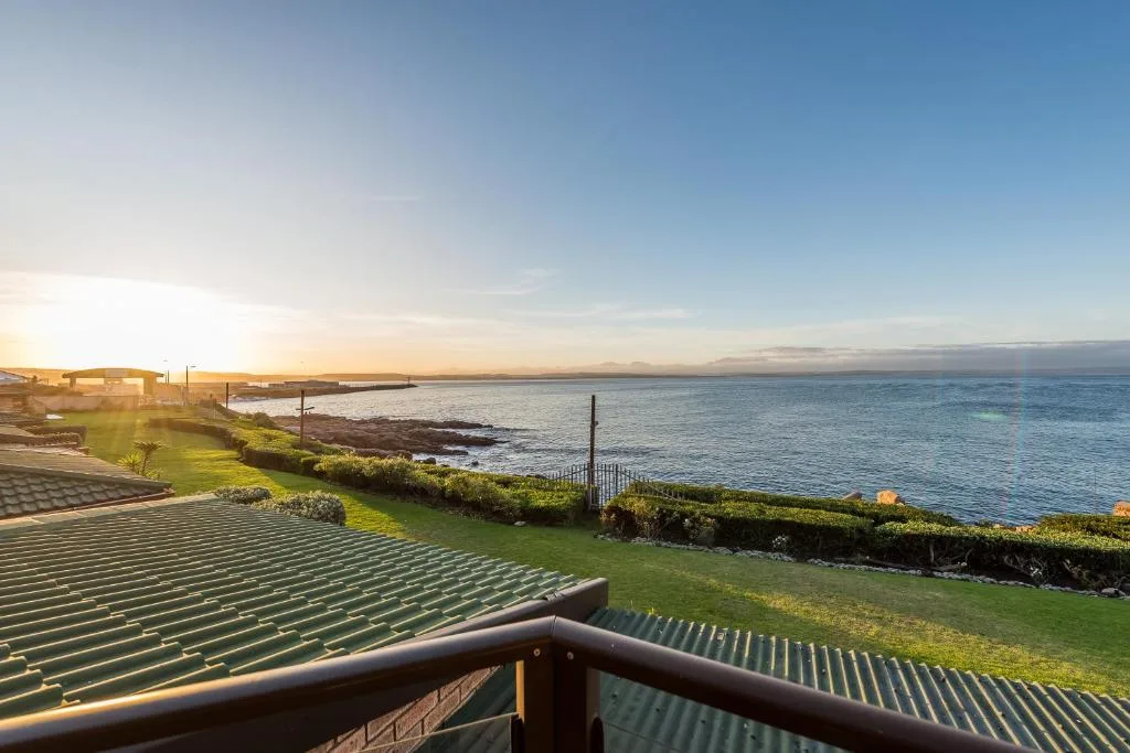 Scenic coastal vista with ocean, manicured lawn, and distant mountains at sunset