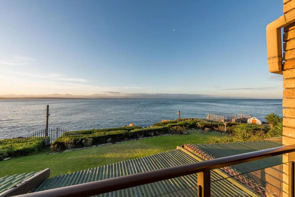 Expansive ocean view from deck with manicured lawn and distant mountains