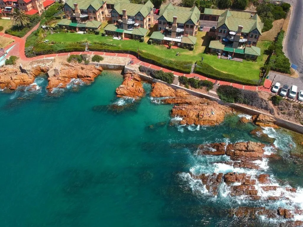 Turquoise ocean waters and rocky coastline with luxury seaside properties on green lawns