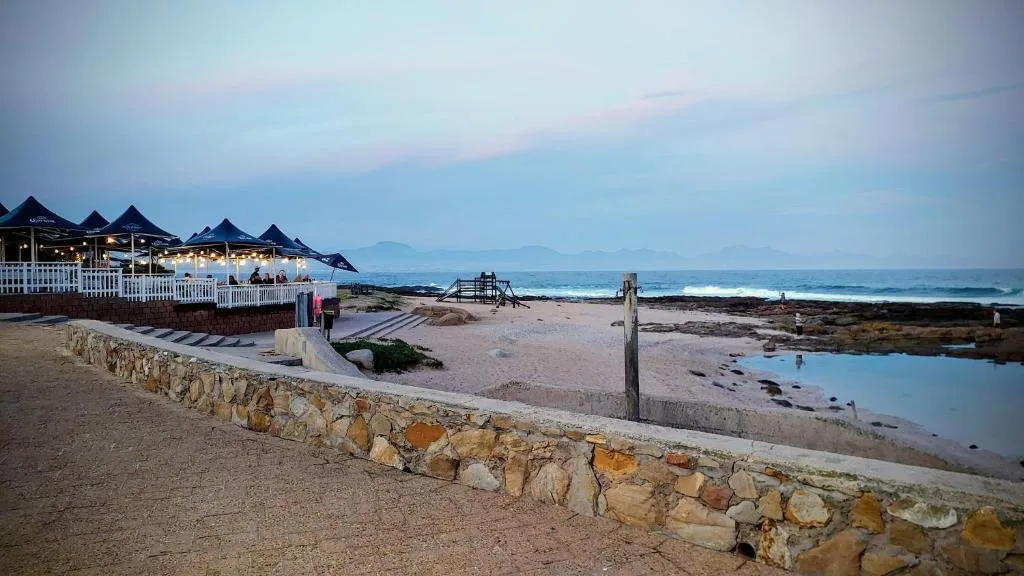 Beachfront property at sunset with ocean, mountains, and beach pavilion
