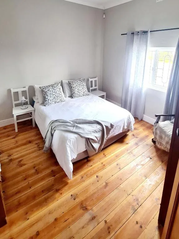 Bright bedroom with queen bed, white bedding, patterned pillows, wooden floors
