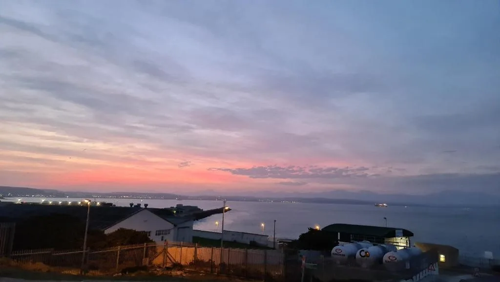 Scenic sunset over Mossel Bay lagoon with distant mountains and coastal lights