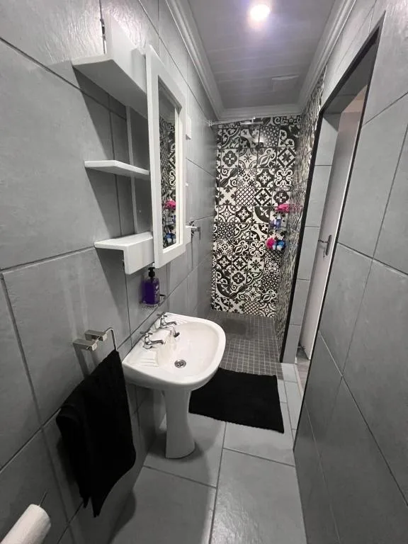 Modern bathroom with pedestal sink, tiled shower, and patterned feature wall