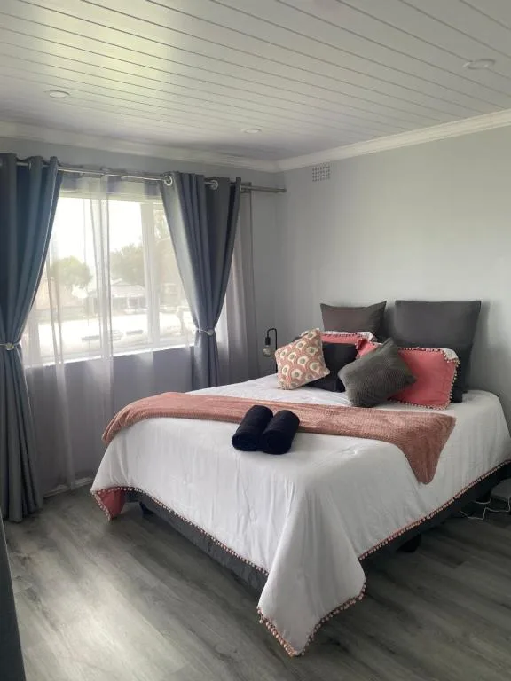 Bright bedroom with queen bed, pink and grey bedding, large windows overlooking garden