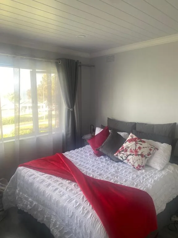 Bright bedroom with queen bed, red throw, and garden view through glass doors