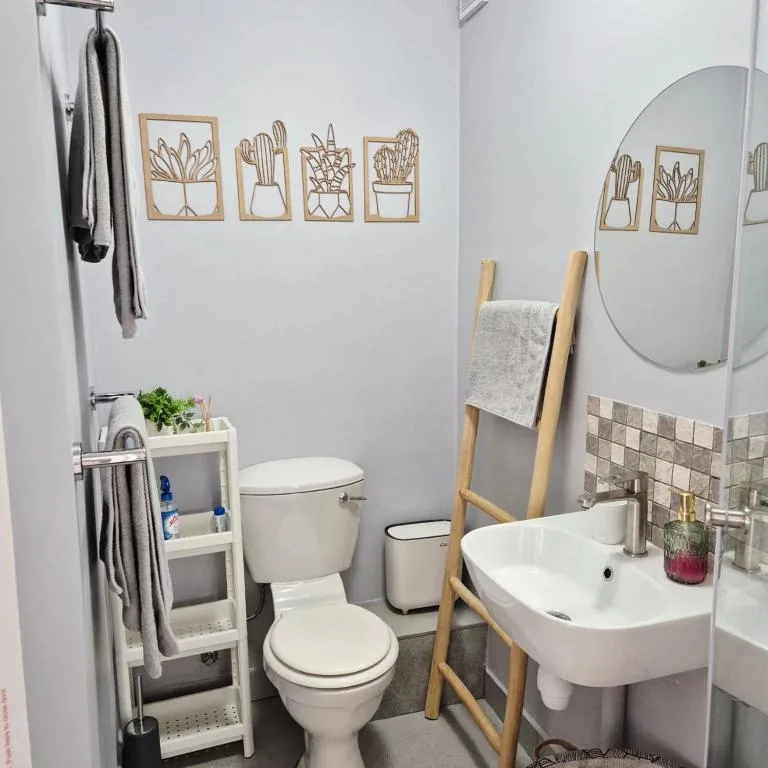 Modern bathroom with white sink, toilet, mirror, and decorative plant wall art