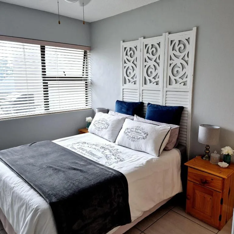 Bright bedroom with queen bed, blue pillows, wooden nightstand, decorative headboard